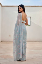 Woman wearing a light blue saree with floral patterns in an outdoor setting. Product by Umaid Couture.