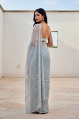 Woman wearing a light blue saree with floral patterns in an outdoor setting. Product by Umaid Couture.