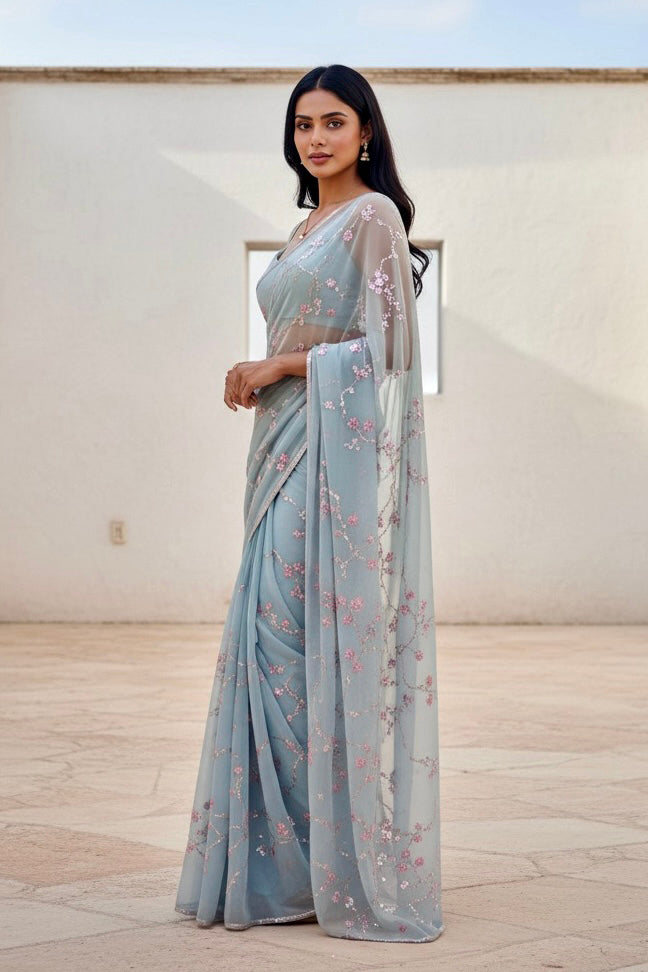 Woman wearing a light blue saree with floral patterns indoors. Product by Umaid Couture.
