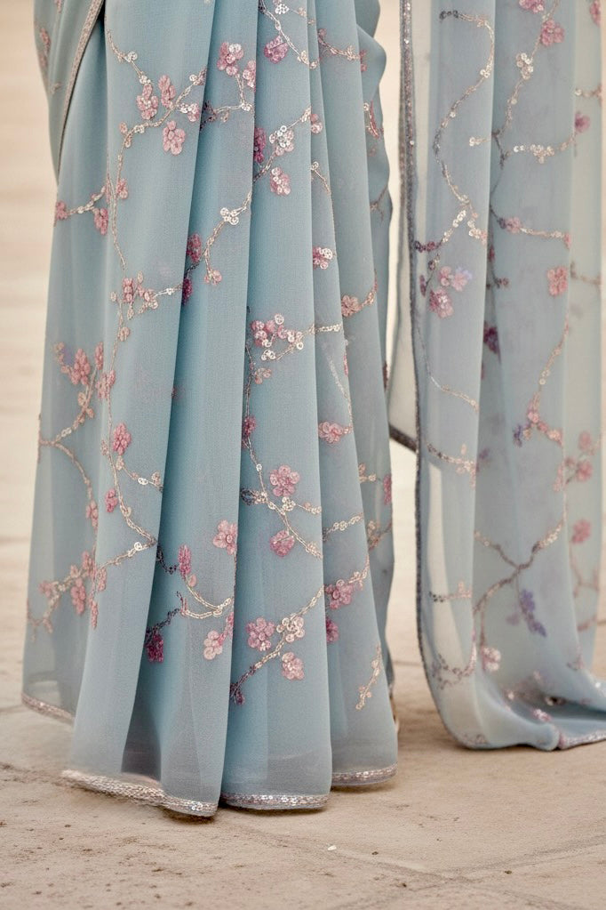 Light blue fabric with floral embroidery on a wooden floor. Product by Umaid Couture.