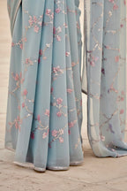 Light blue fabric with floral embroidery on a wooden floor. Product by Umaid Couture.