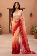 Woman wearing a beige and red saree with floral patterns indoors. Product by Umaid Couture.