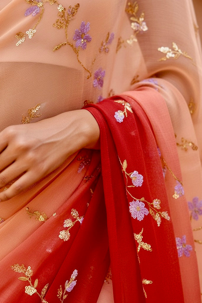 Close-up of a person wearing a saree with floral embroidery in red and beige. Product by Umaid Couture.