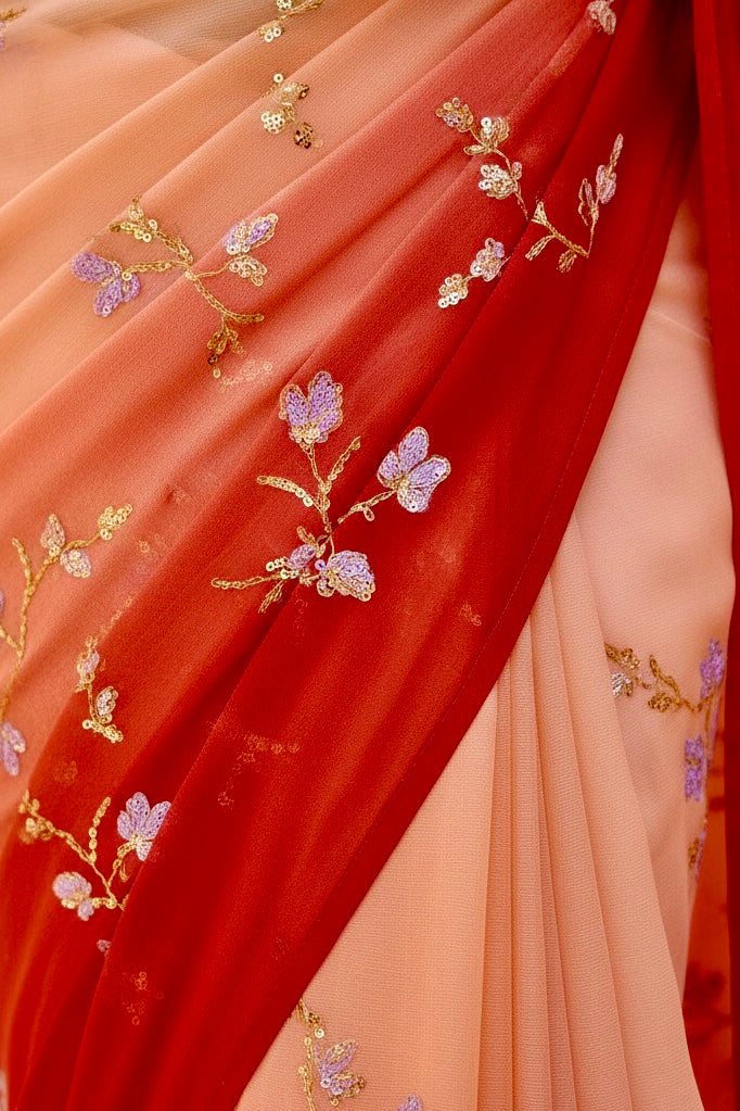 Close-up of a saree with intricate gold and purple floral embroidery on a peach and red background.. Product by Umaid Couture.