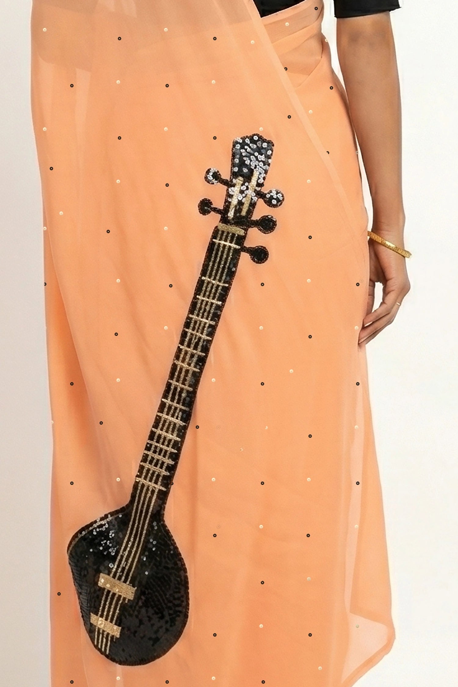 An Indian woman in peach Ragini Saree embellished  with Sitar Motifs made of Zari & sequins by craft of Aari-Zardosi, a product of Umaid Couture